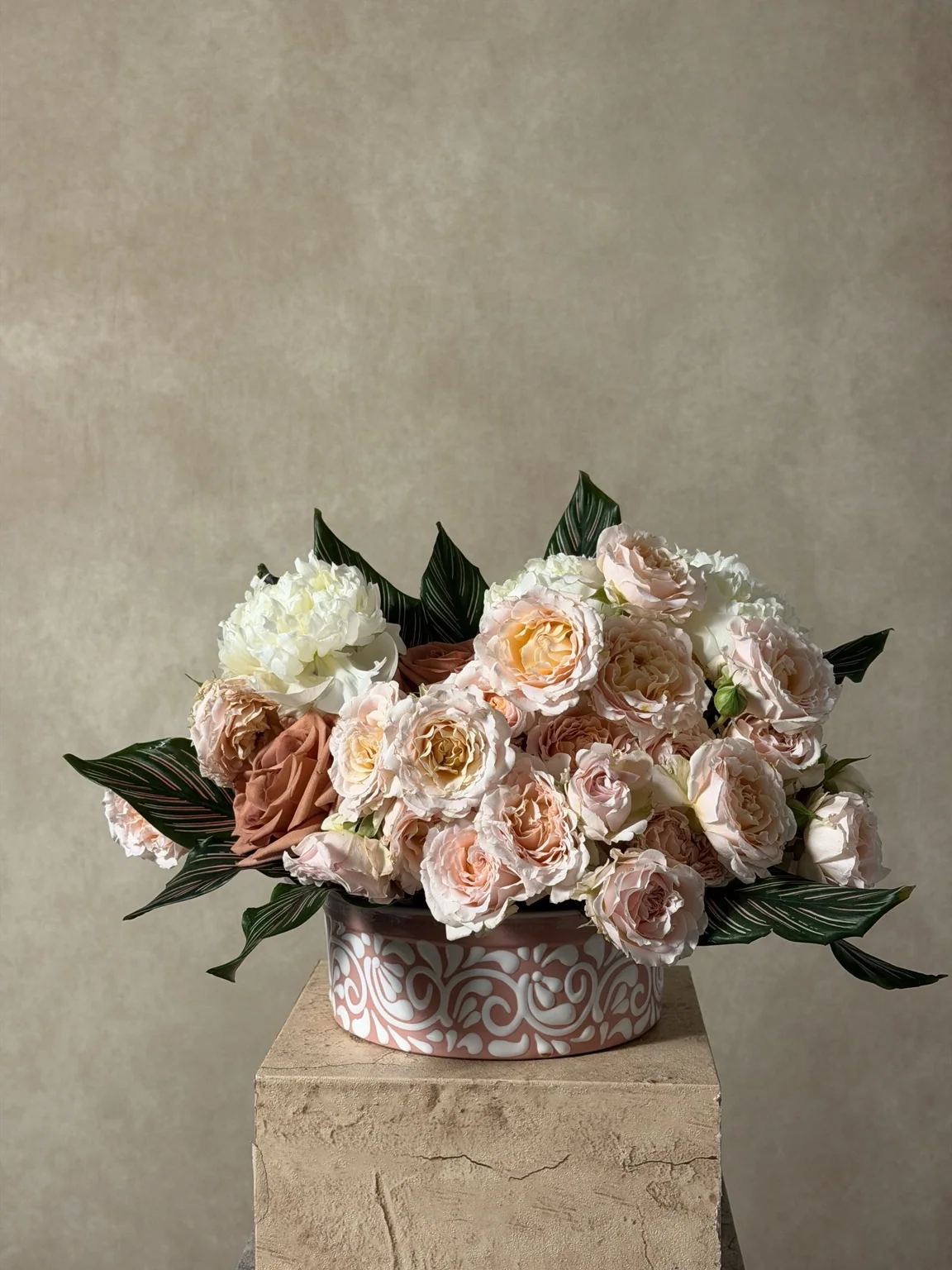 Peach garden roses and white peonies in a patterned ceramic bowl