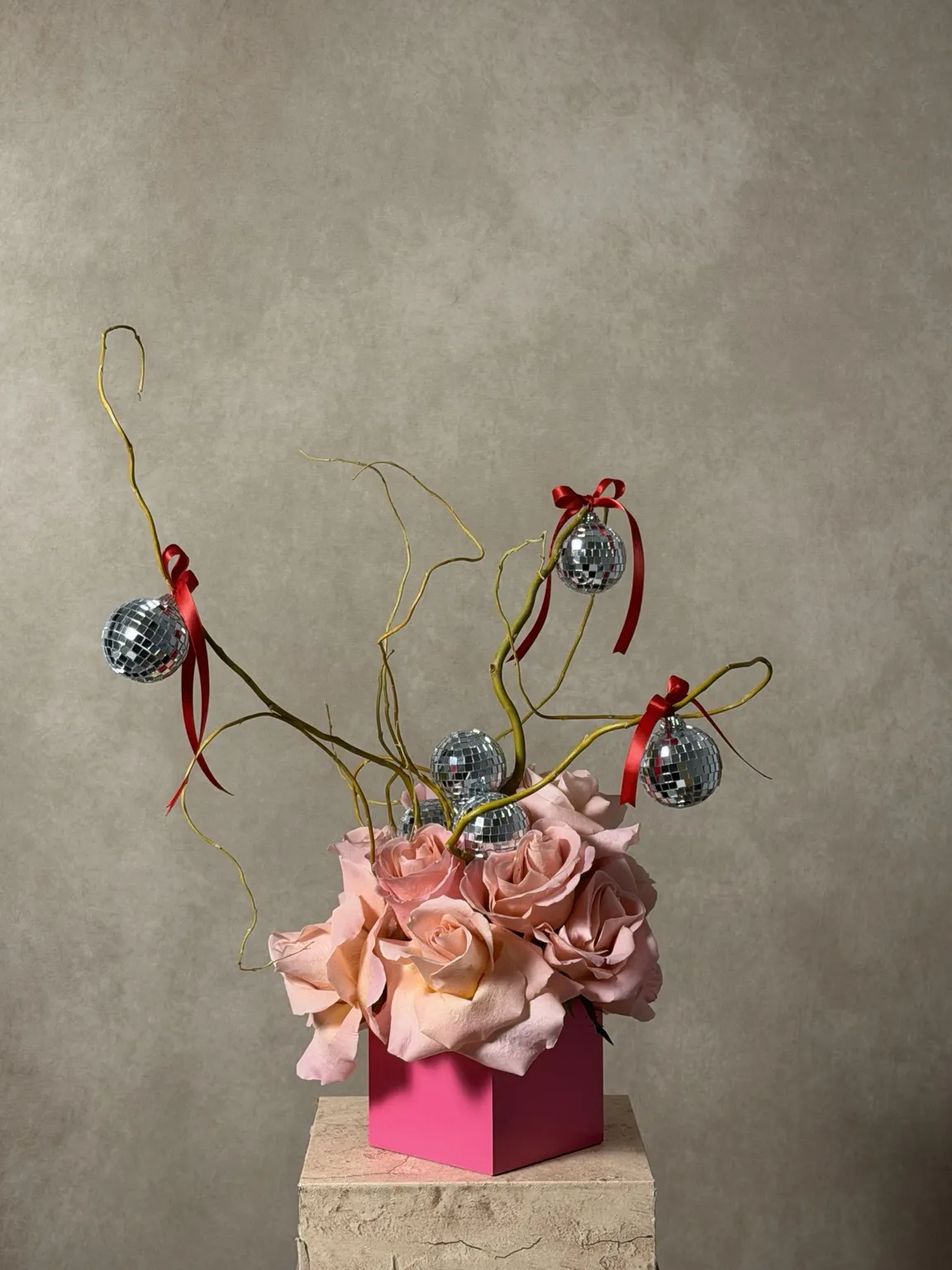 Pink roses in a hot pink cube with curly willow, red ribbons and hanging mirror balls