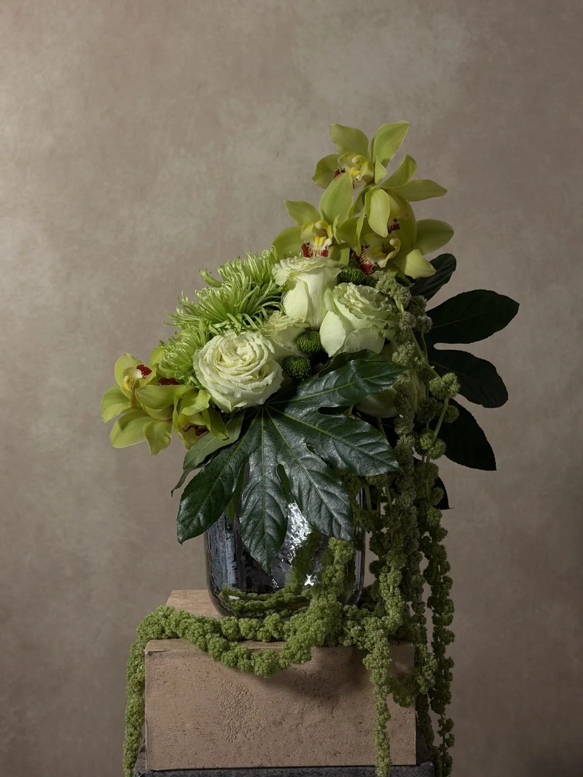 Green cymbidium orchids, white roses and hanging green amaranthus in a glass vase