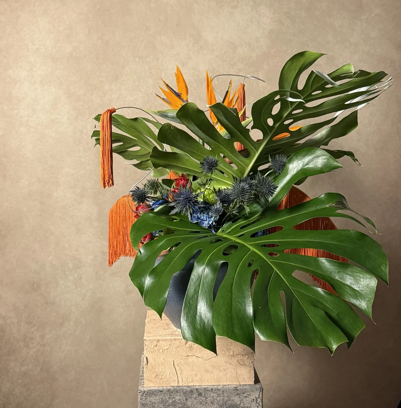 Side view of the fashion week sculpture showing a monstera leaf sweeping over the vessel and an orange tassel