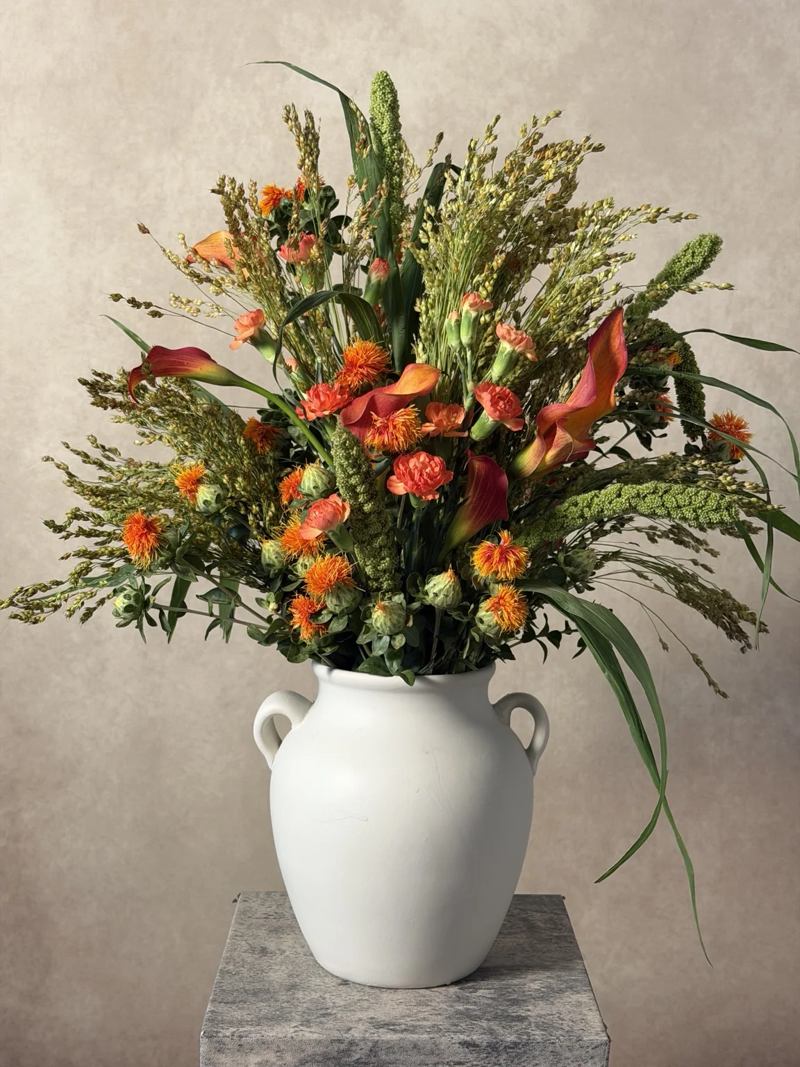 Orange carnations, lilies and wild grasses in a white jug