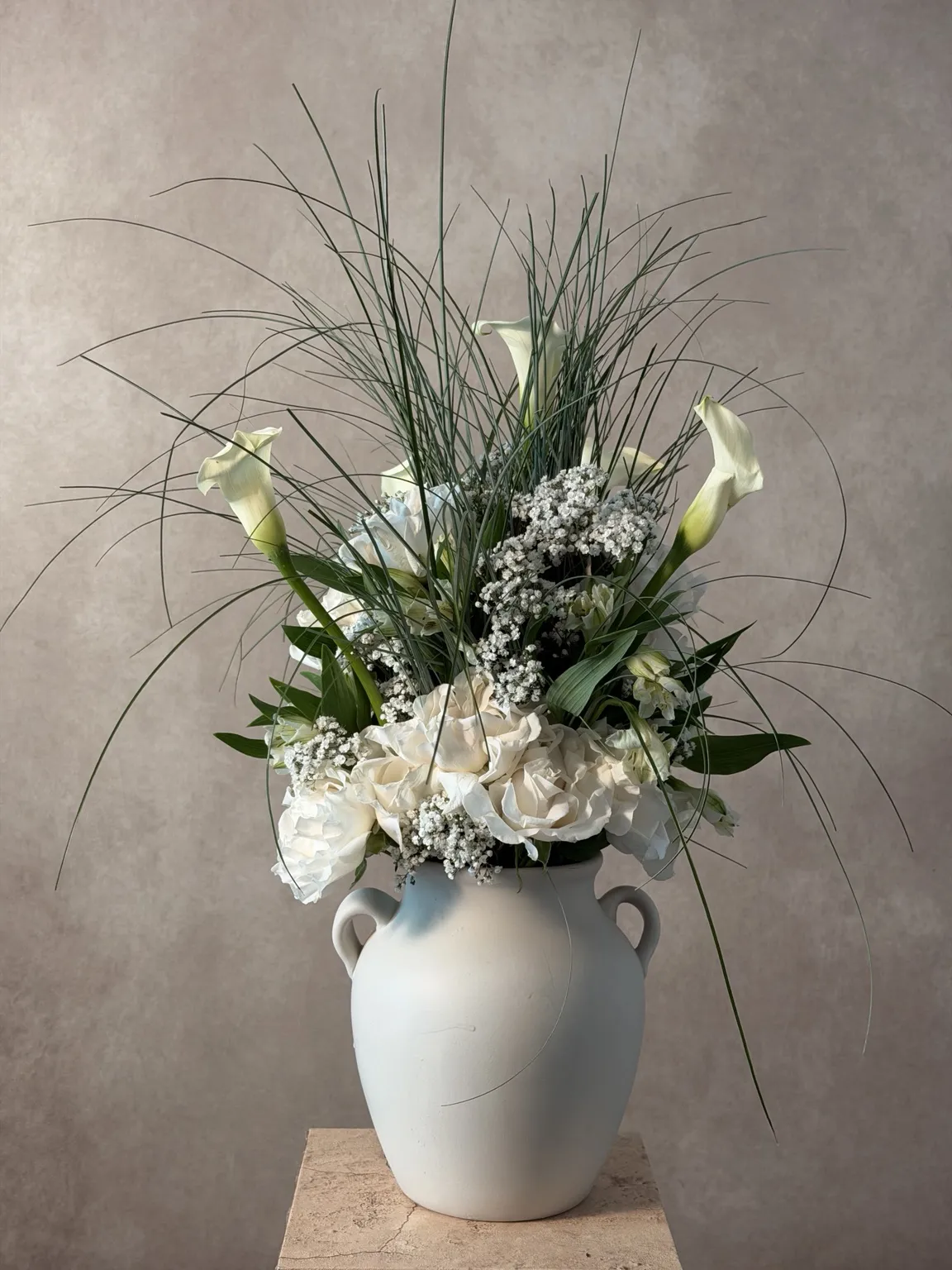 White calla lilies, hydrangea and fine grasses in a white ceramic amphora