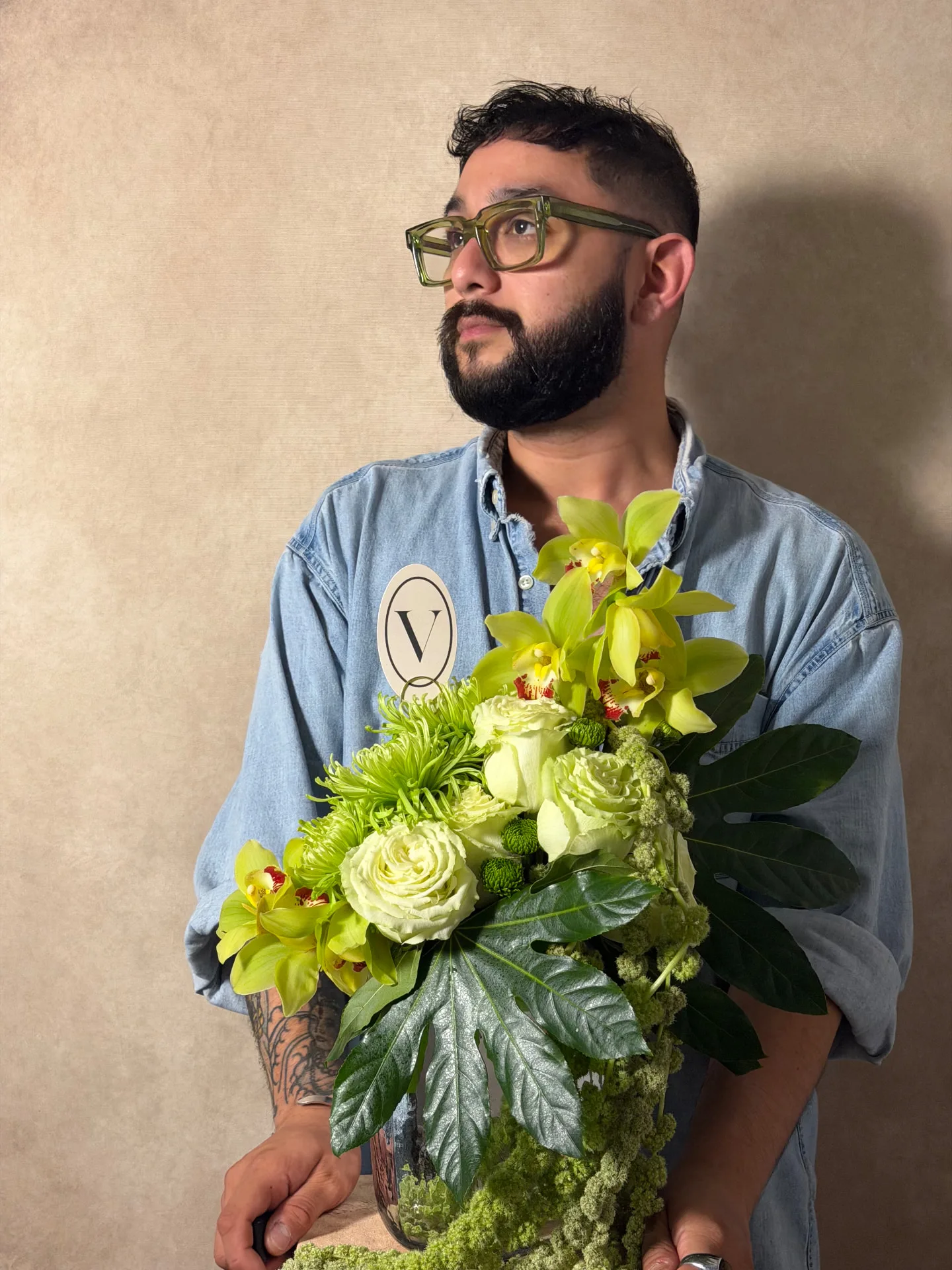 Ivan holding an arrangement of lime cymbidium orchids, cream roses, green spider mums and fatsia leaves against a beige wall