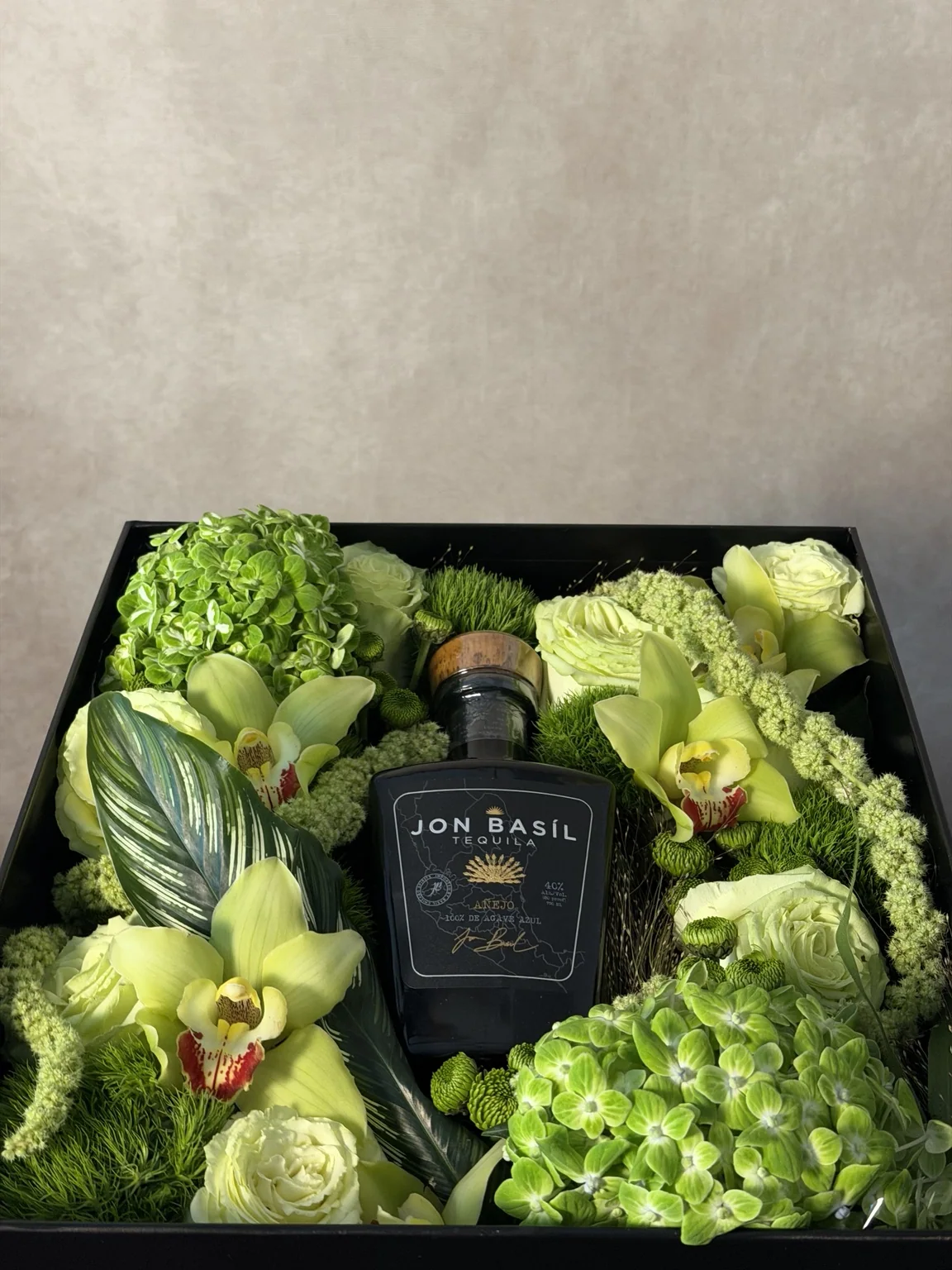 Black box of green orchids, roses and hydrangea around a tequila bottle