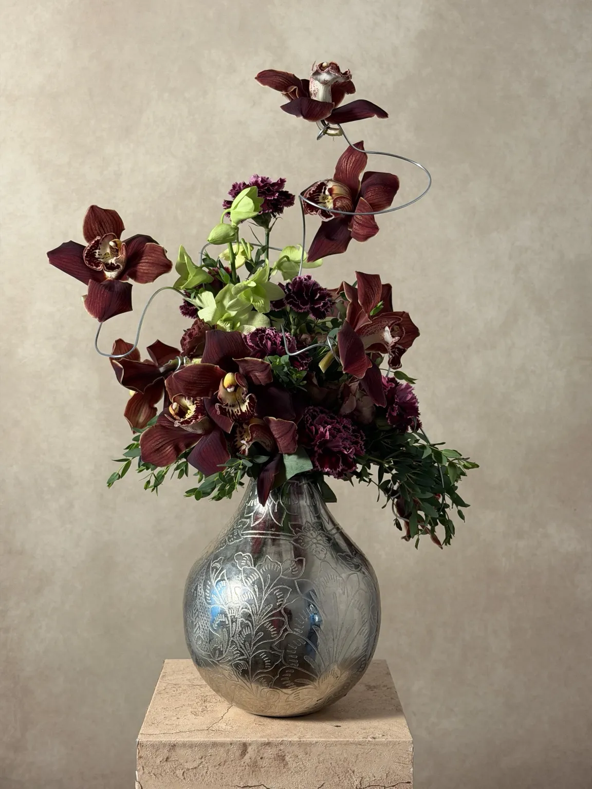 Burgundy cymbidium orchids on looping wire above a mercury-glass vase