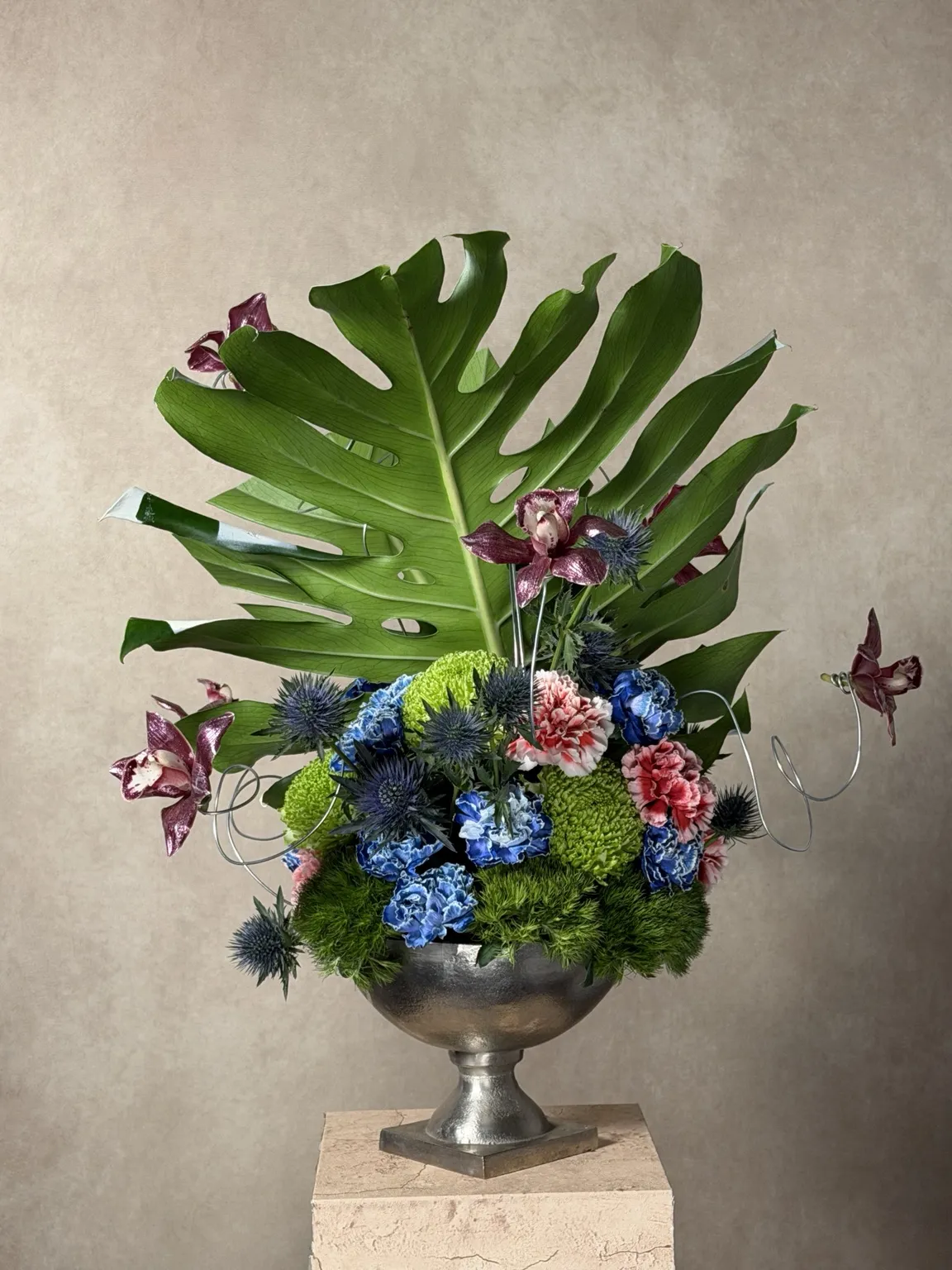 Back of the silver-vessel piece showing a green monstera leaf, orchids on wire and blue hydrangea