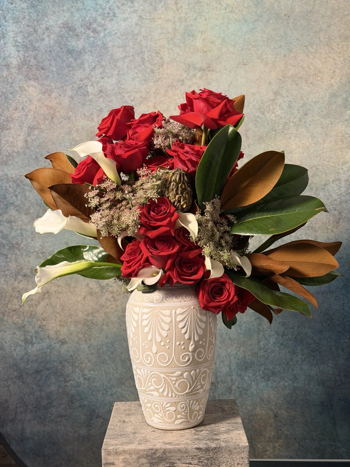 Red roses, magnolia leaves and calla lilies in a carved white vase