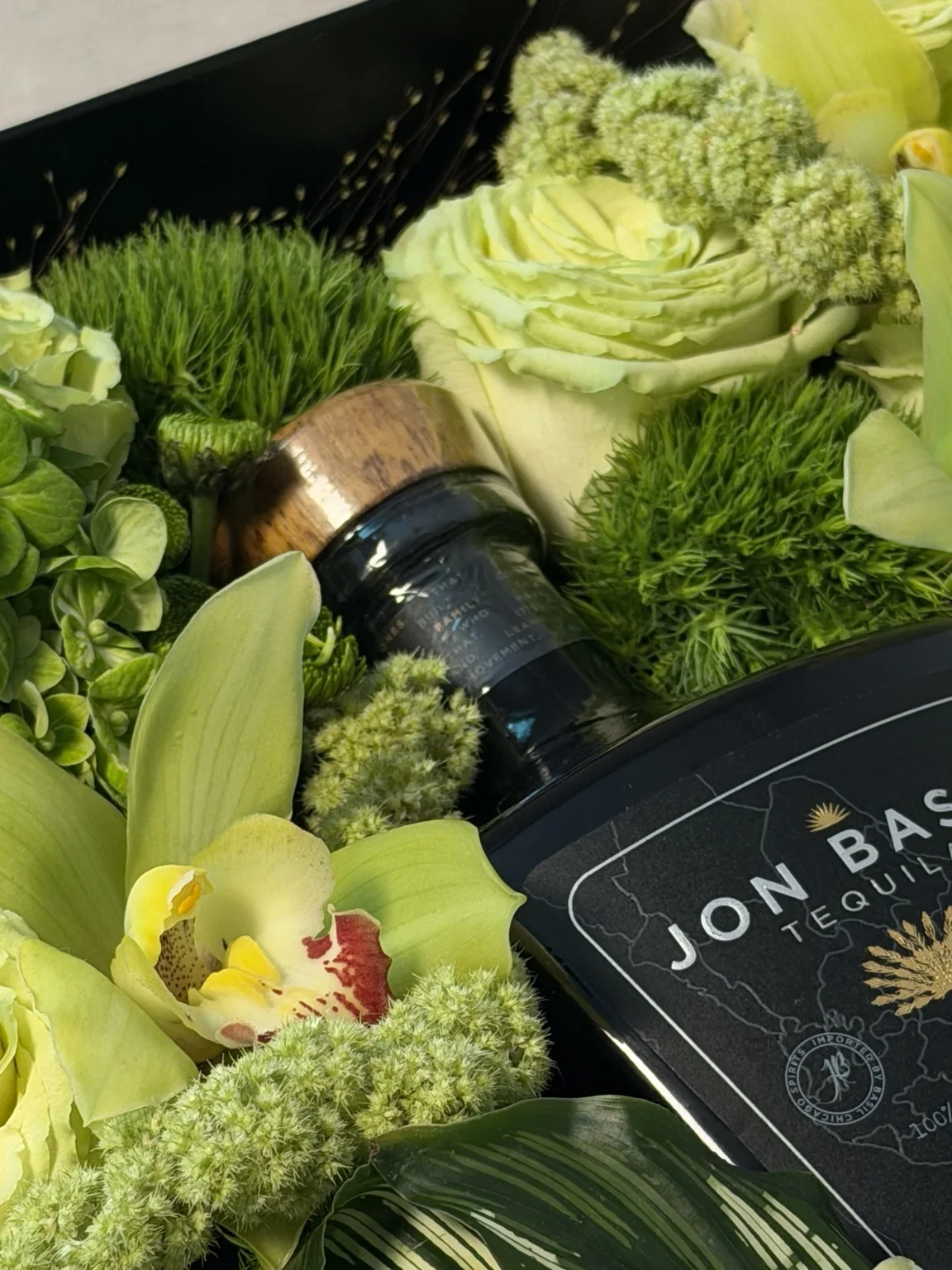 Close detail of green roses and orchids beside the tequila bottle