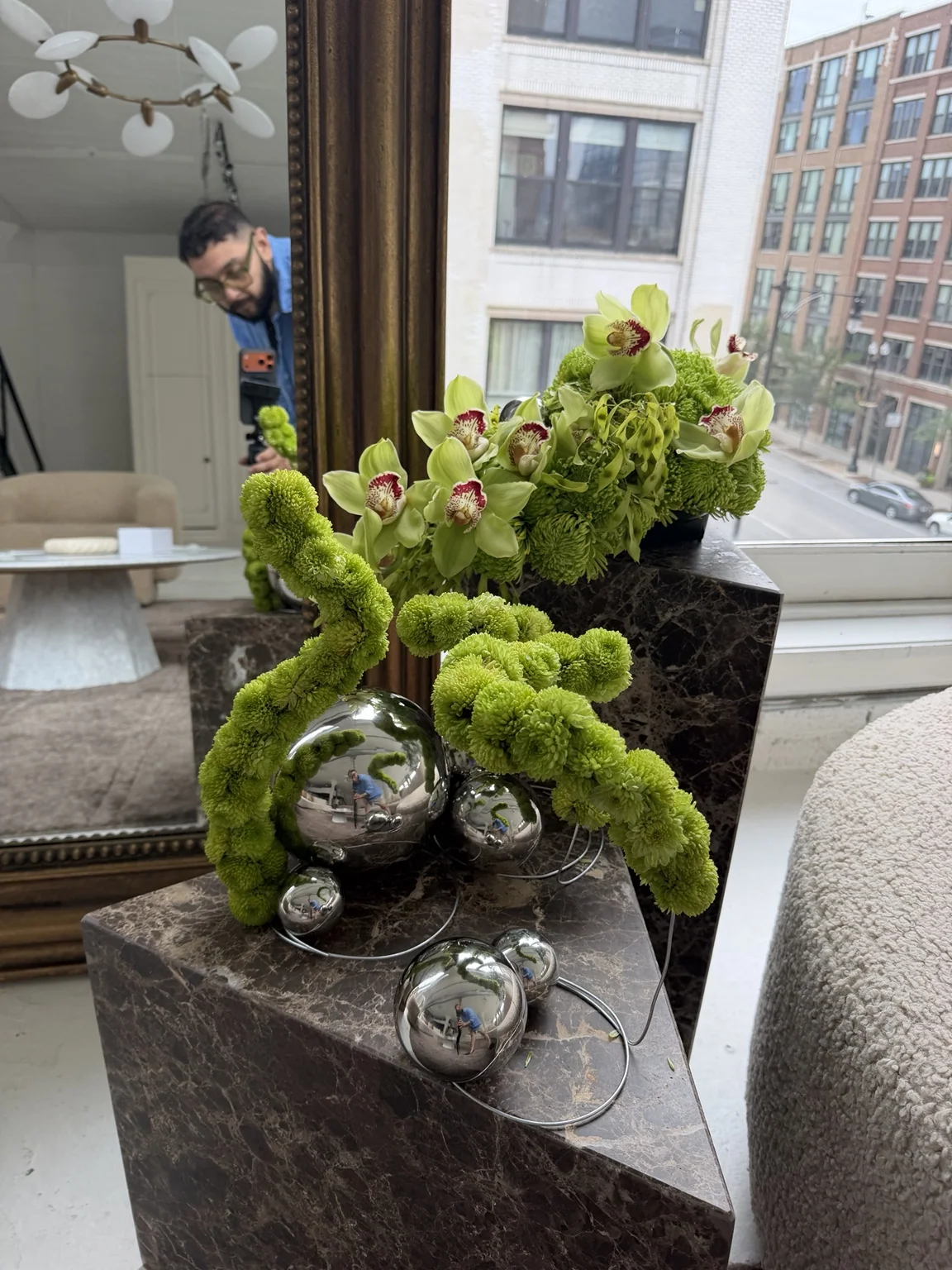 Green cymbidium orchids and chrome spheres on a dark stone plinth