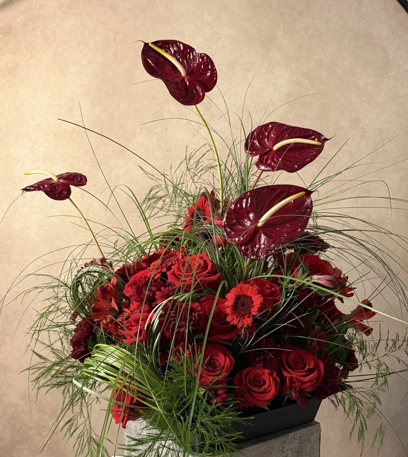 Red anthuriums rising above red roses and fine grasses